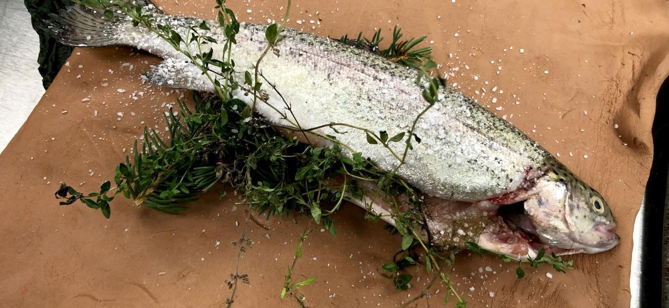 Local New York trout salted and packed with herbs on a clay slab. The trout is wrapped in the wet clay and baked in the oven. Chef Maricela Vega at Hartwick College Fall 2022.  Image Credit Stephanie A. Rozene