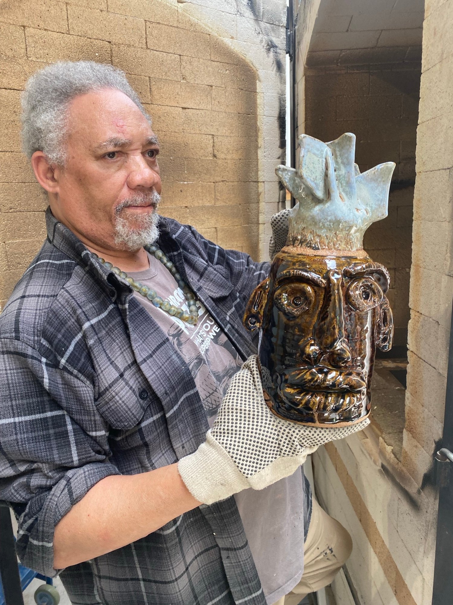Jim McDowel beside his kiln, holding Church Lady face jug, 2025, photo credit Jan Fisher.