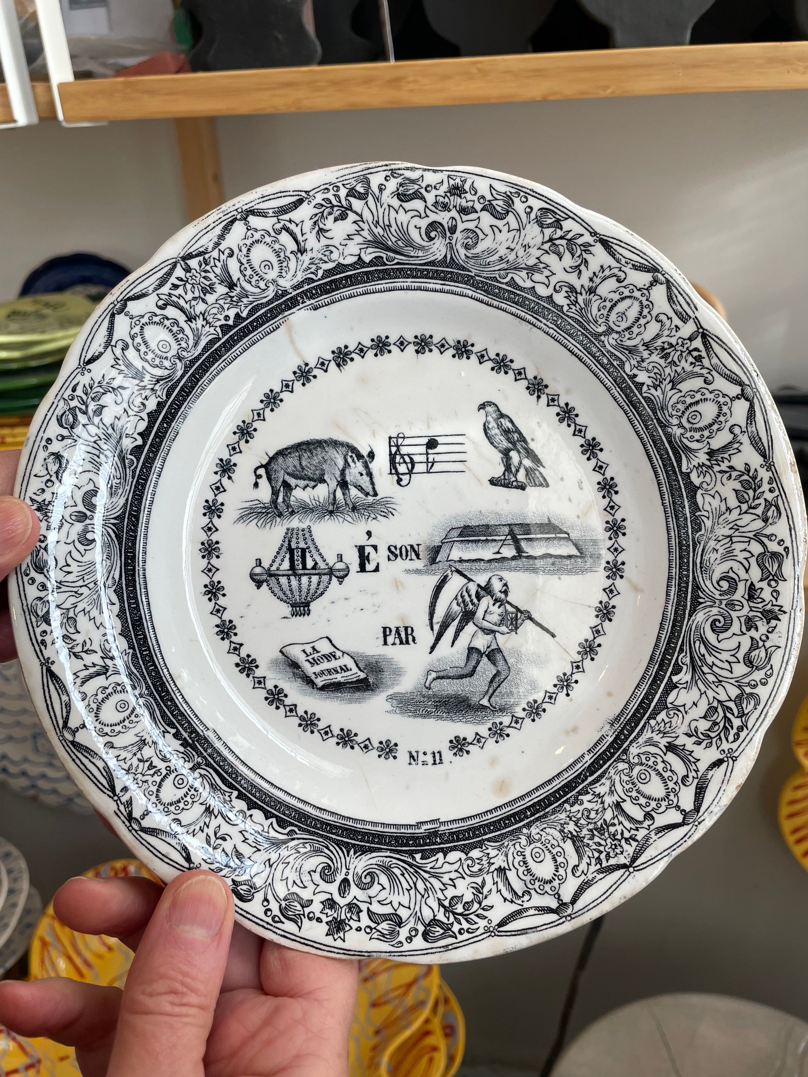 For the Curious – The Inspiration. Dessert Plate. transferware, “Porcelaine Opaque de Gien”, France, late 19th C 19.8 cn (7.8 in) diameter   Reverse: “Les Rebus illustres sont fort a la mode par le Temps qui court.” French rebuses are “sounds like” rather than “spelled like”- Portrayed is a female boar so not sanglier, but laie; the method of naming musical notes using syllables is called solfège – this is the musical note ré; in France a buzzard /hawk is buse; IL on the lustre (chandelier);  fort (like a fort itself) means strong; the letter A applies to the next image – the journal La Mode; finally, the figure of father time running (time is running out or how time flies).